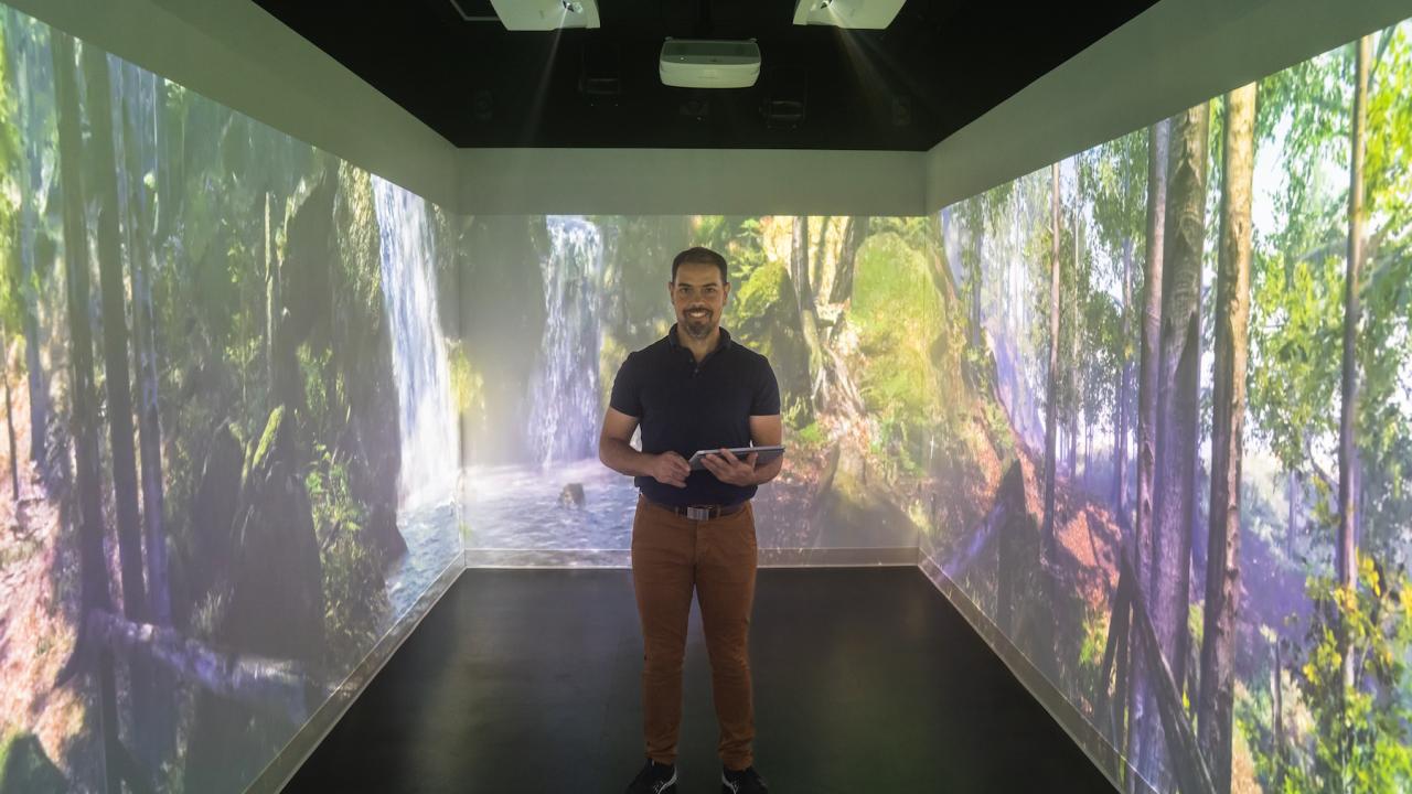 Julien Delarue, associate professor in sensory science, stands in the immersive room. He's surrounded by 4 walls showing video of woods and waterfalls.