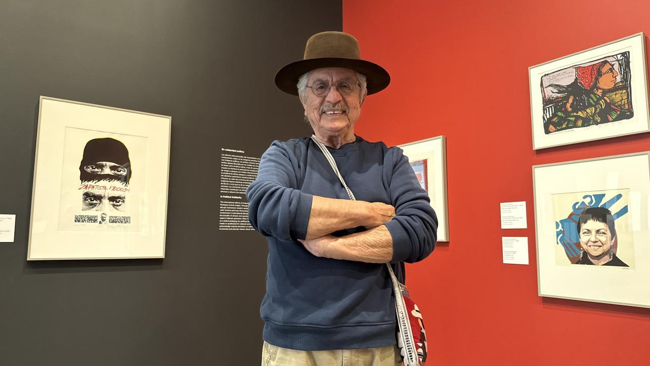 Male artist in hat stands in front of his work in a museum