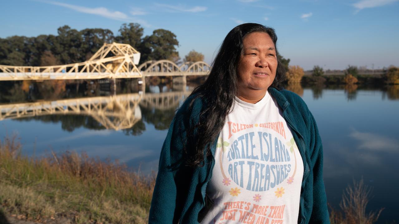 Pam Bulahan iin sweater and t-shirt stands with Sacramento River behind her