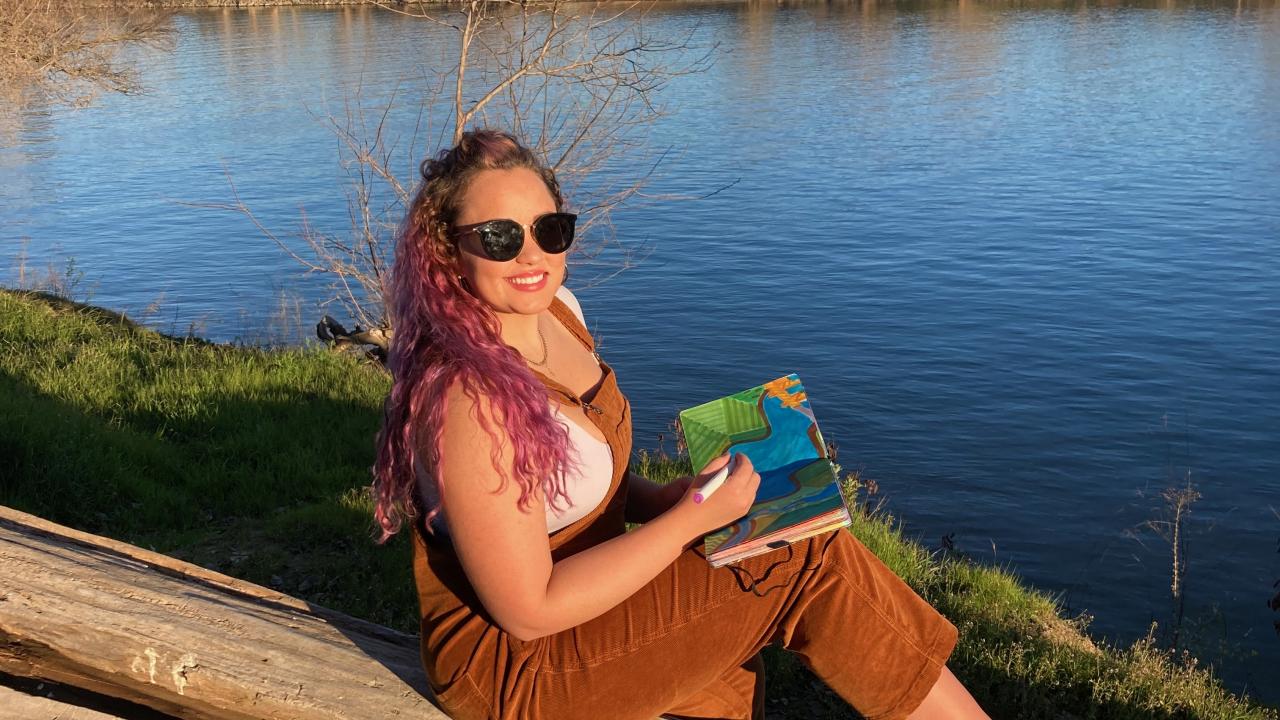 Rachael Dal Porto with sketchbook on log by Sacramento River