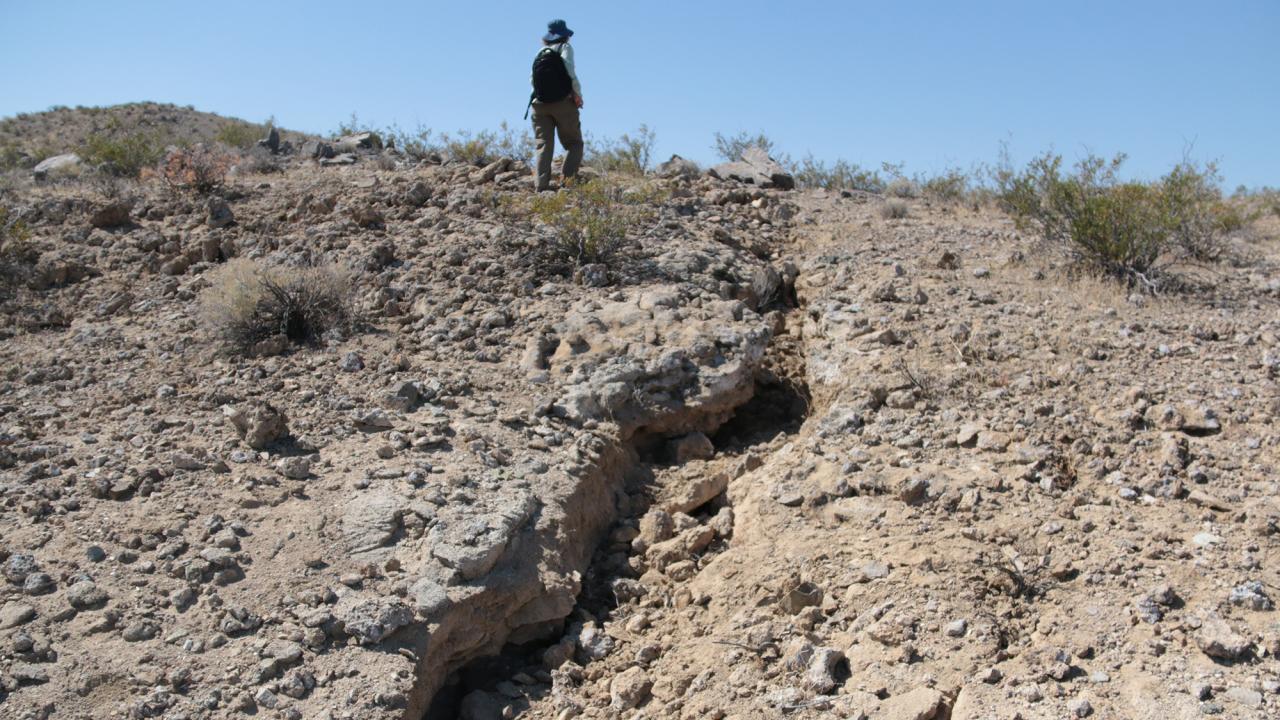 View of cracked earth from earthquake with a geologist in the background