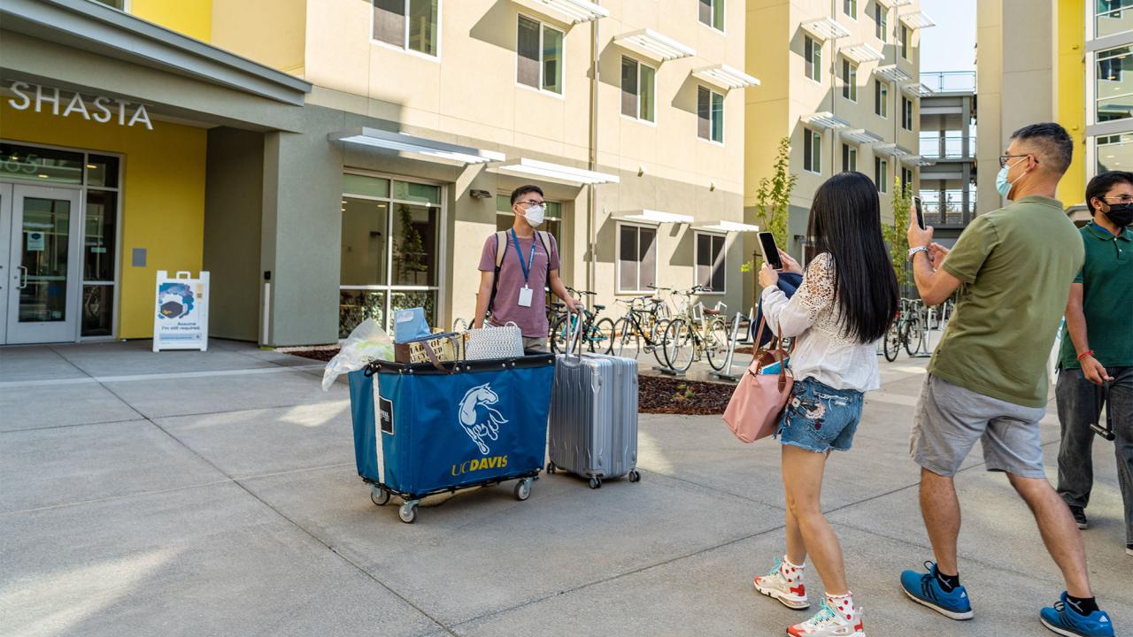 A man and a woman photograph a student with belongings in front of Shasta Hall