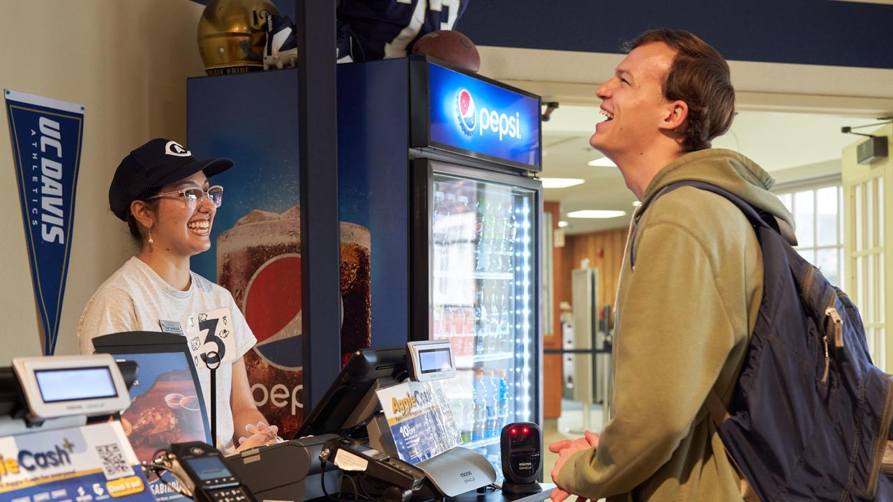 A male student looks up at a menu while the cashier waits for his order