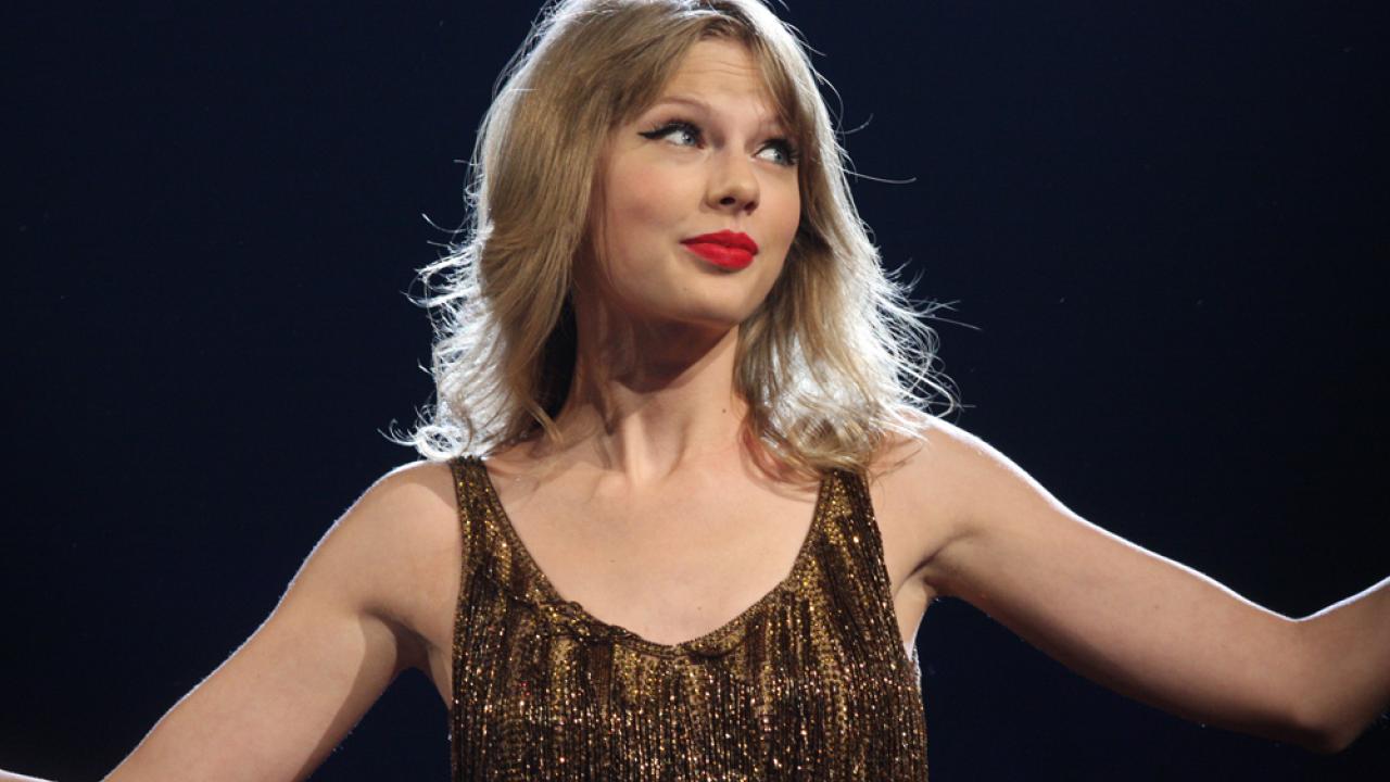 Singer Taylor Swift in sequined top holds arms out with black background