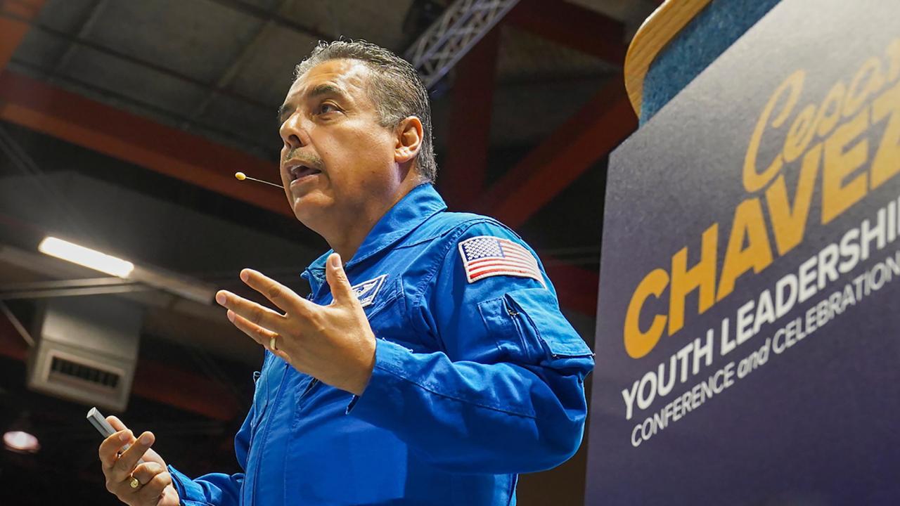 Jose Hernandez in blue NASA uniform with Cesar Chavez event poster in background