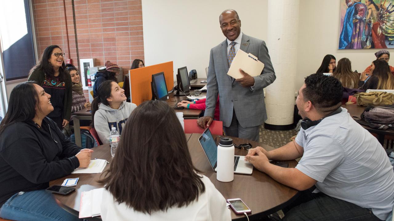 Chancellor Gary S. May, in suit and tie, stands while chatting with students at a round table, in academic success centerh students