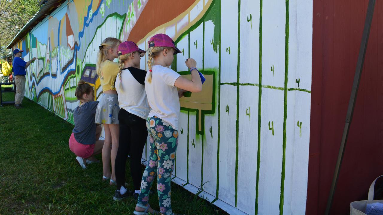 Young girls paint mural on the side of a building.