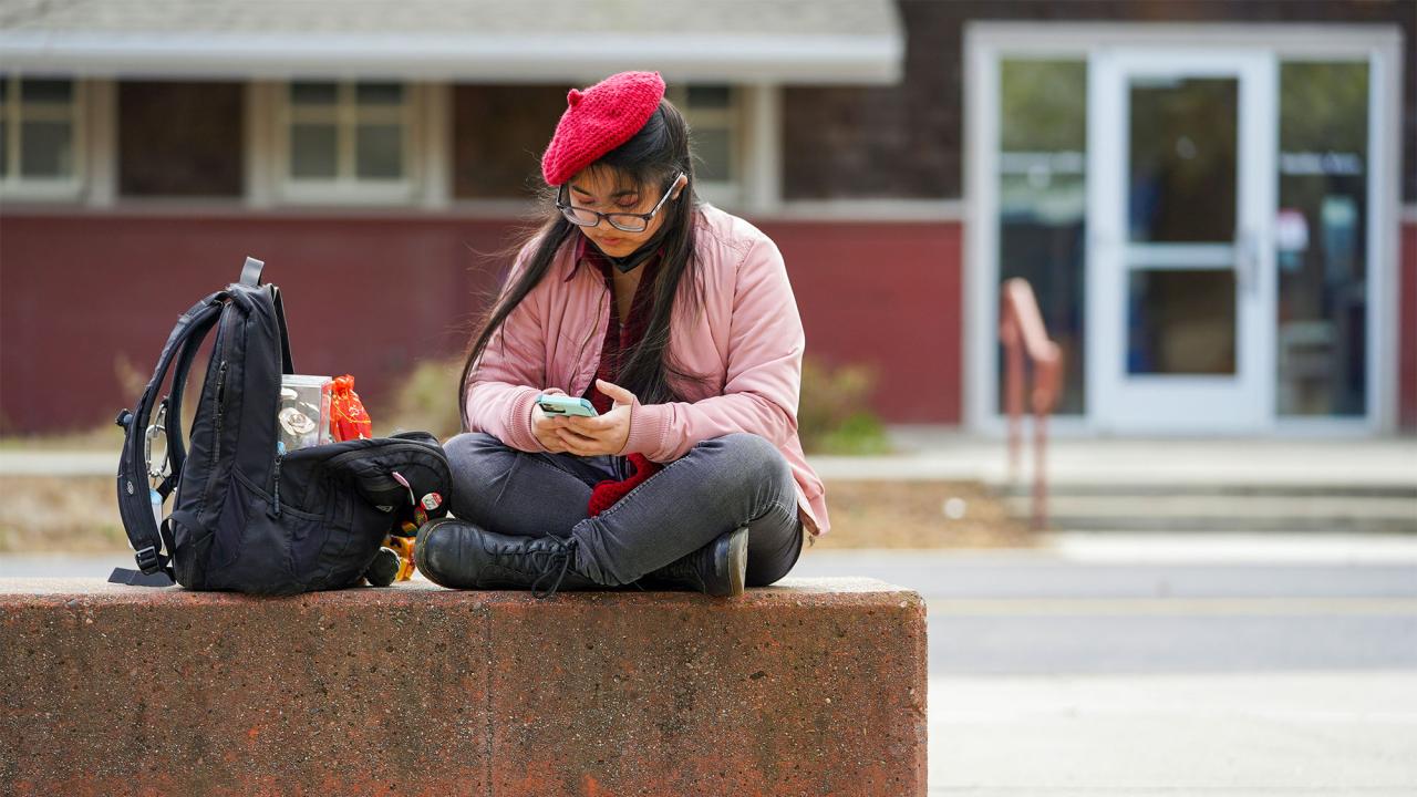 A student wearing a beret uses their smartphone outside of the UC Davis Craft Center.