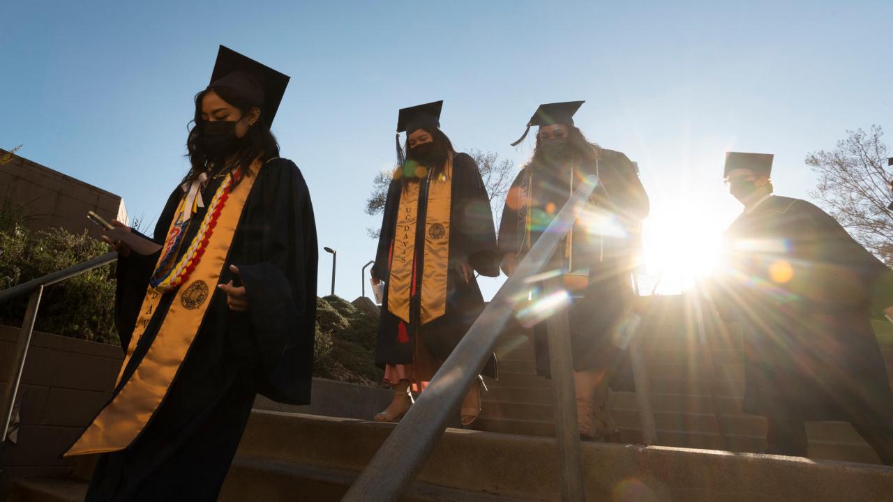 Students in caps and gowns, entering commencement, with sun behind them