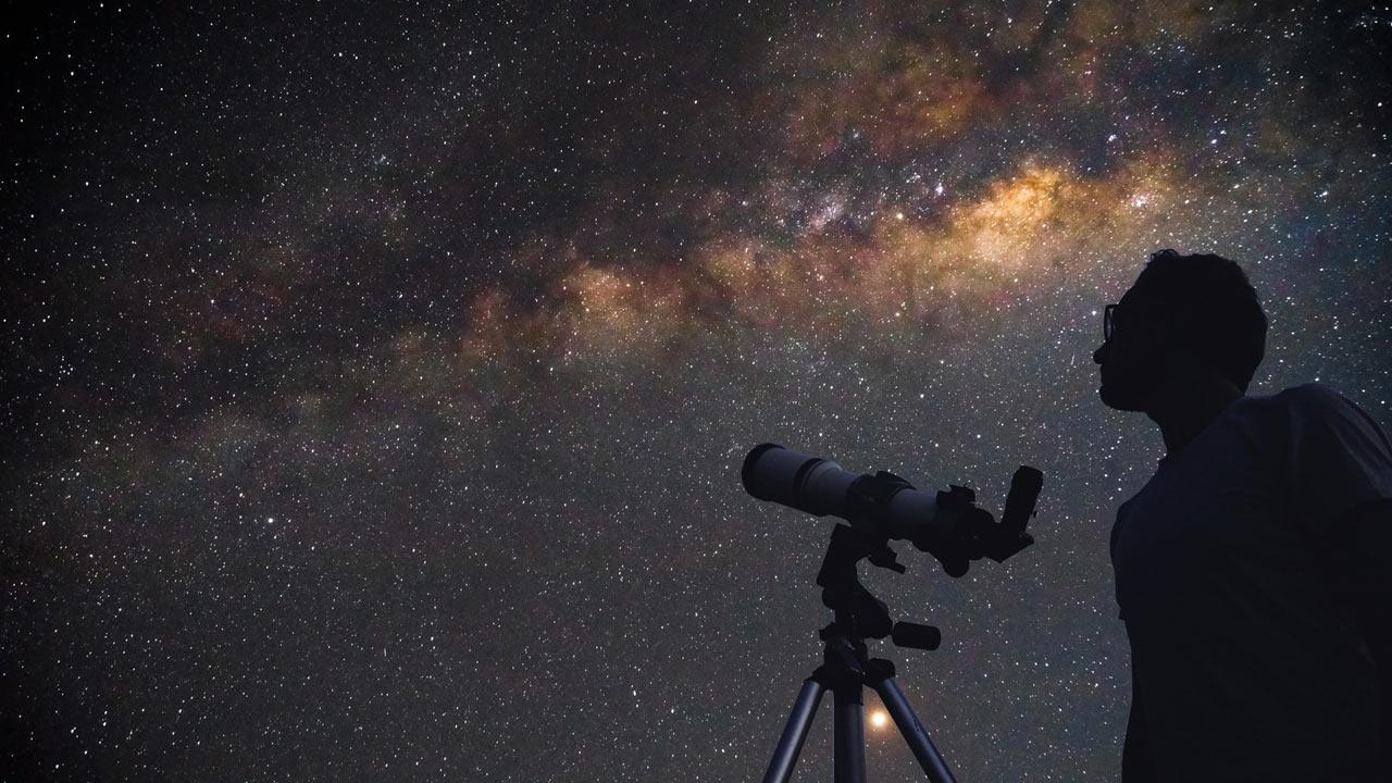 A male looks through a telescope at a starry sky