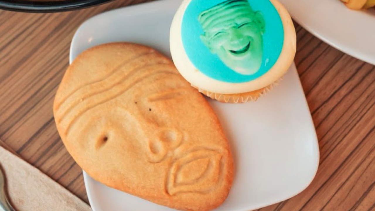 A small plate on a dining commons table holds a sugar cookie in the shape of an Egghead sculpture, Yin & Yang, and a smaller cookie with an edible image of another Egghead sculpture (Eye on Mrak, Fatal Laff)printed on it.