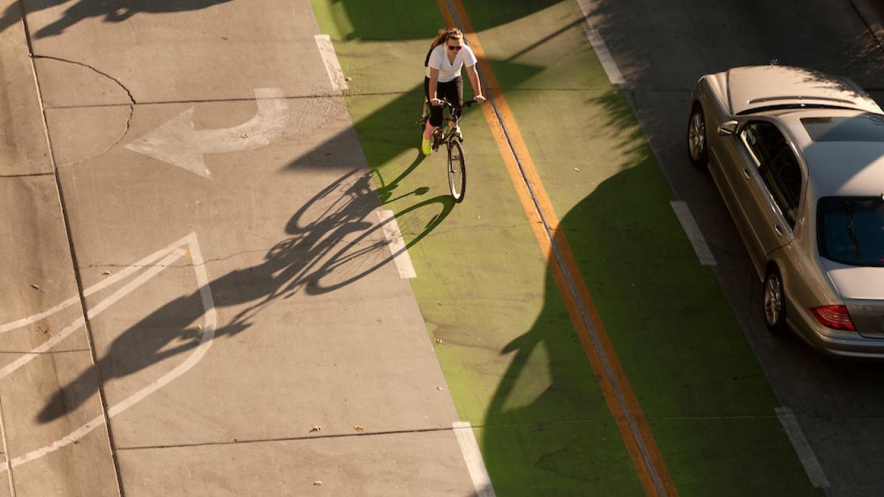 a female student rides her bike through a clearly marked green bike line next to a car on the UC Davis campus