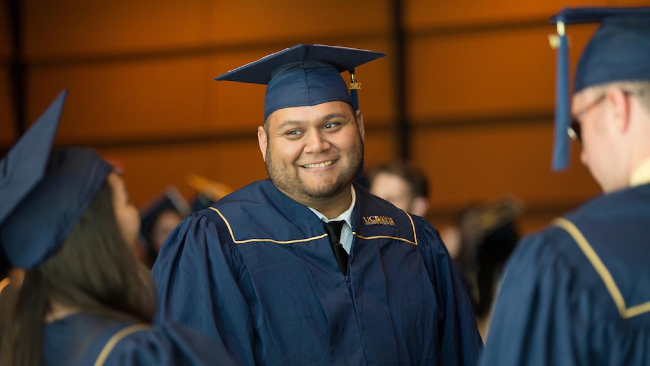A student smiles among friends in his cap and gown at UC Davis. 