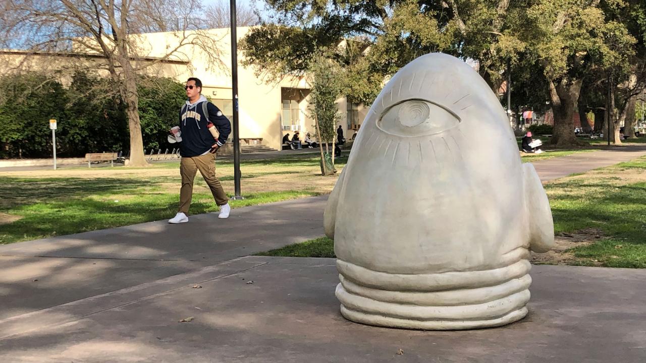 Person walks by the "Eye on Mrak" Egghead sculpture