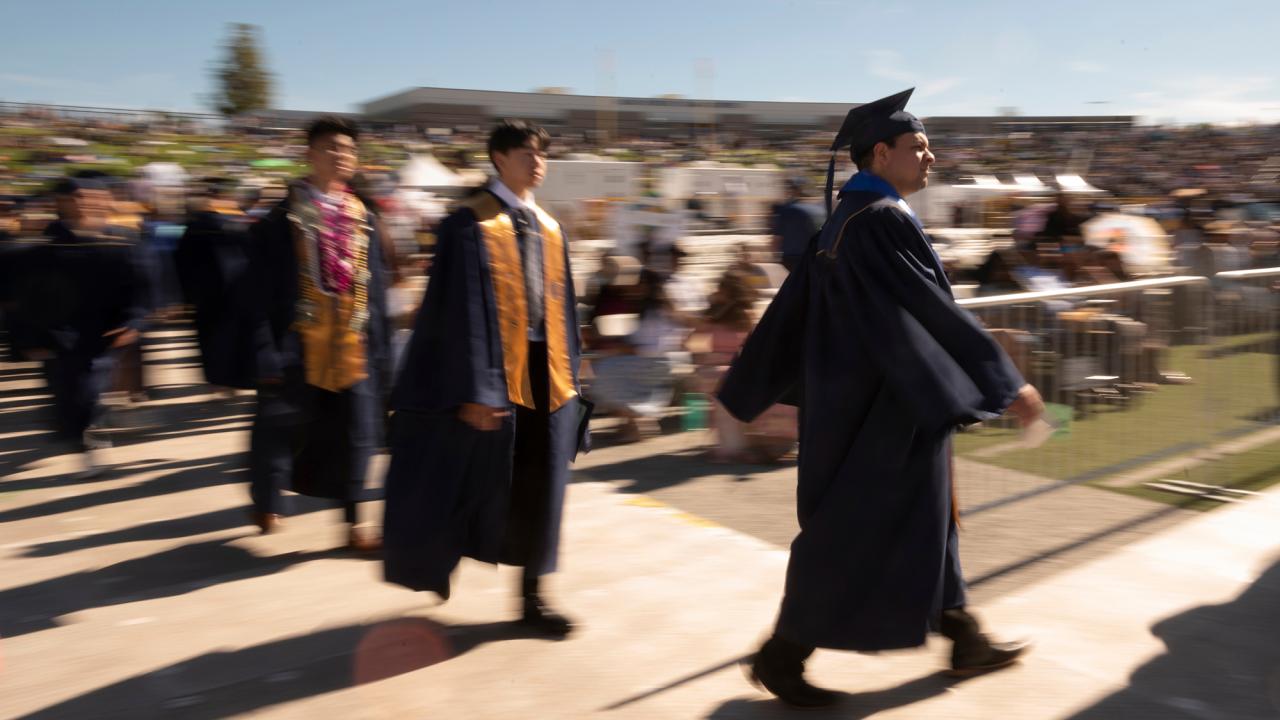 A line of students in graduation regalia enters UC Davis Health Stadium.