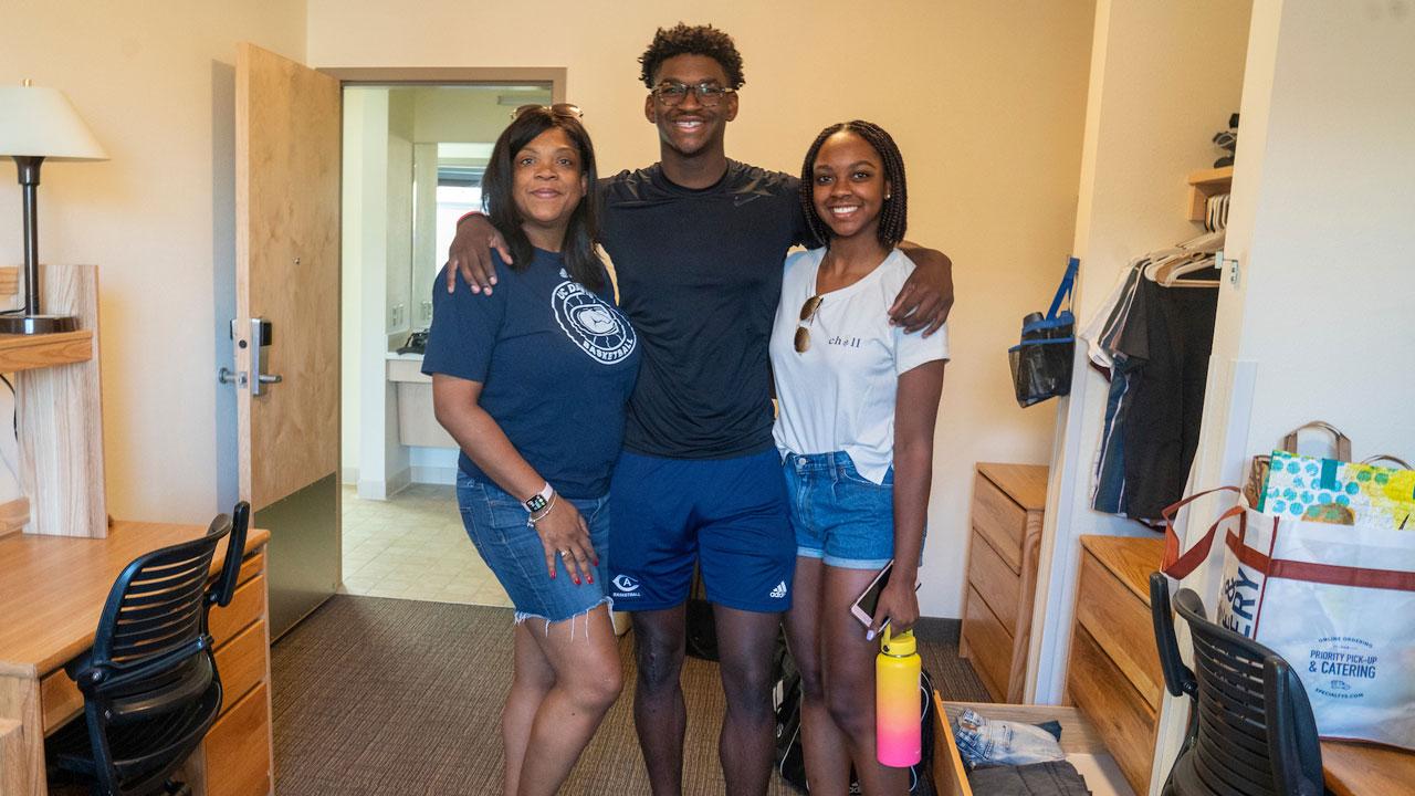 A new student smiles with his family as he moves into his residence hall.