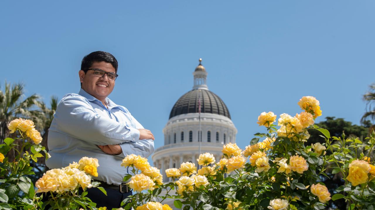 A student poses in front of the state capitol dome and yellow roses. 