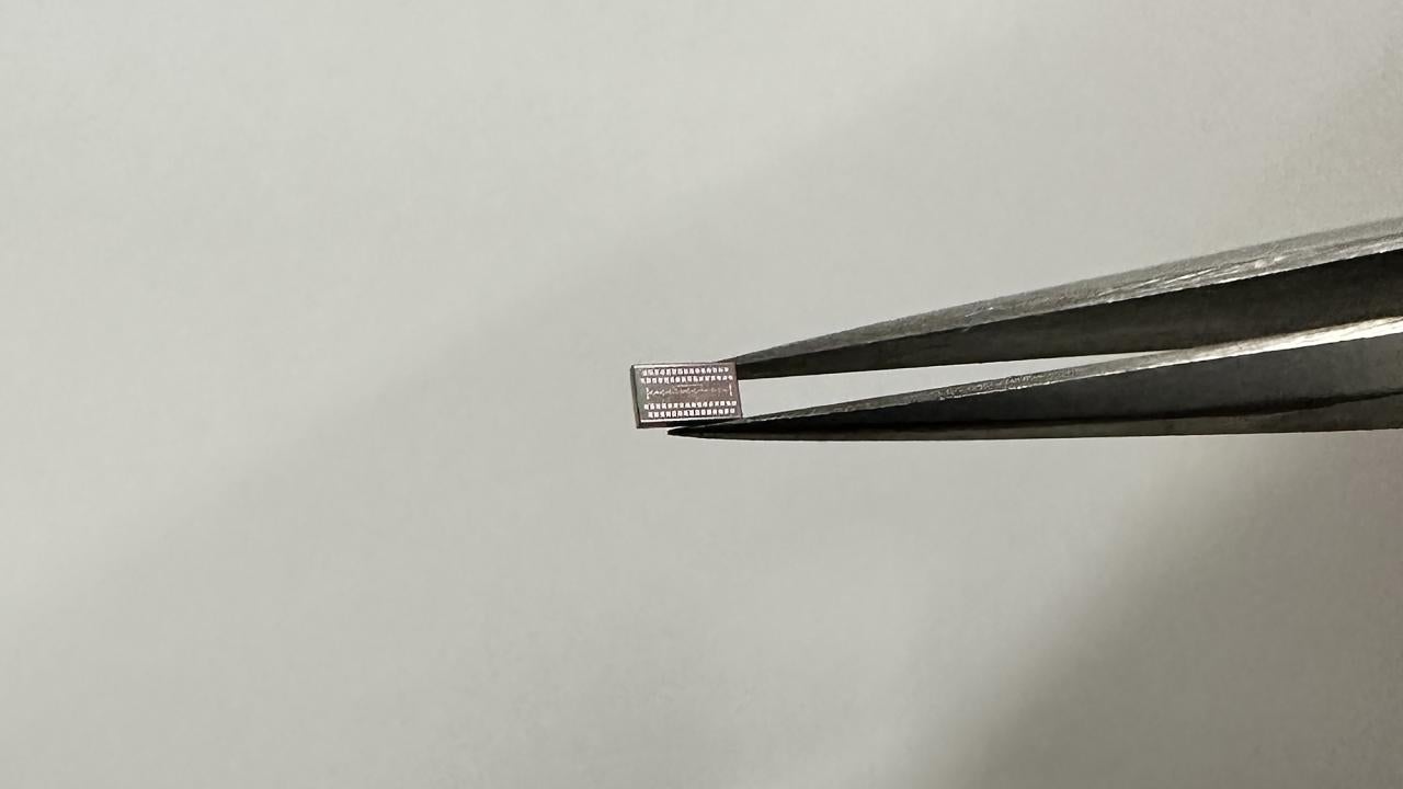 A metal rectangle is held in a pair of tweezers entering from the right. 