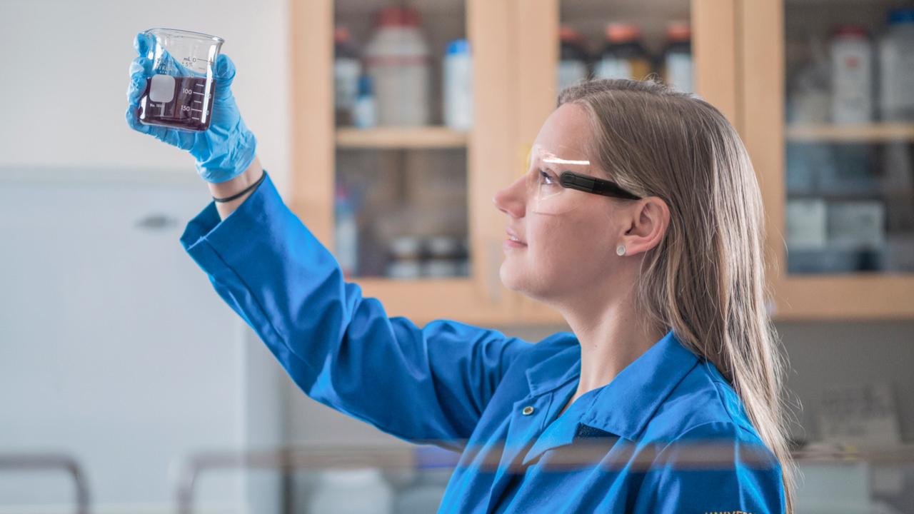 female scientist in lab with blue coat looking at water sample