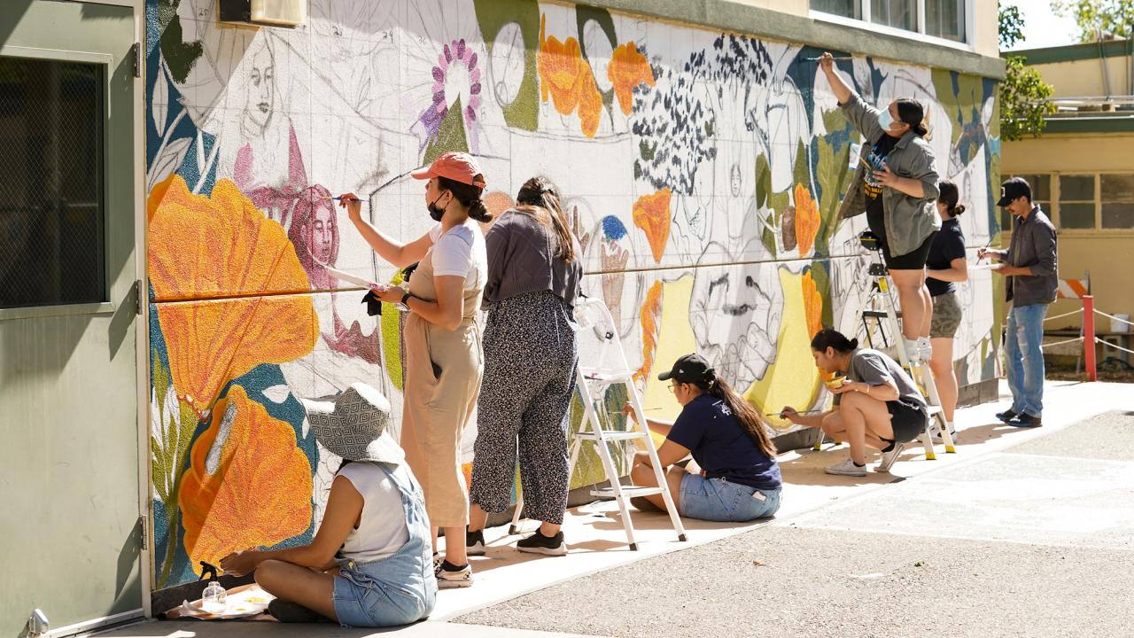 Students paint a mural on a school building