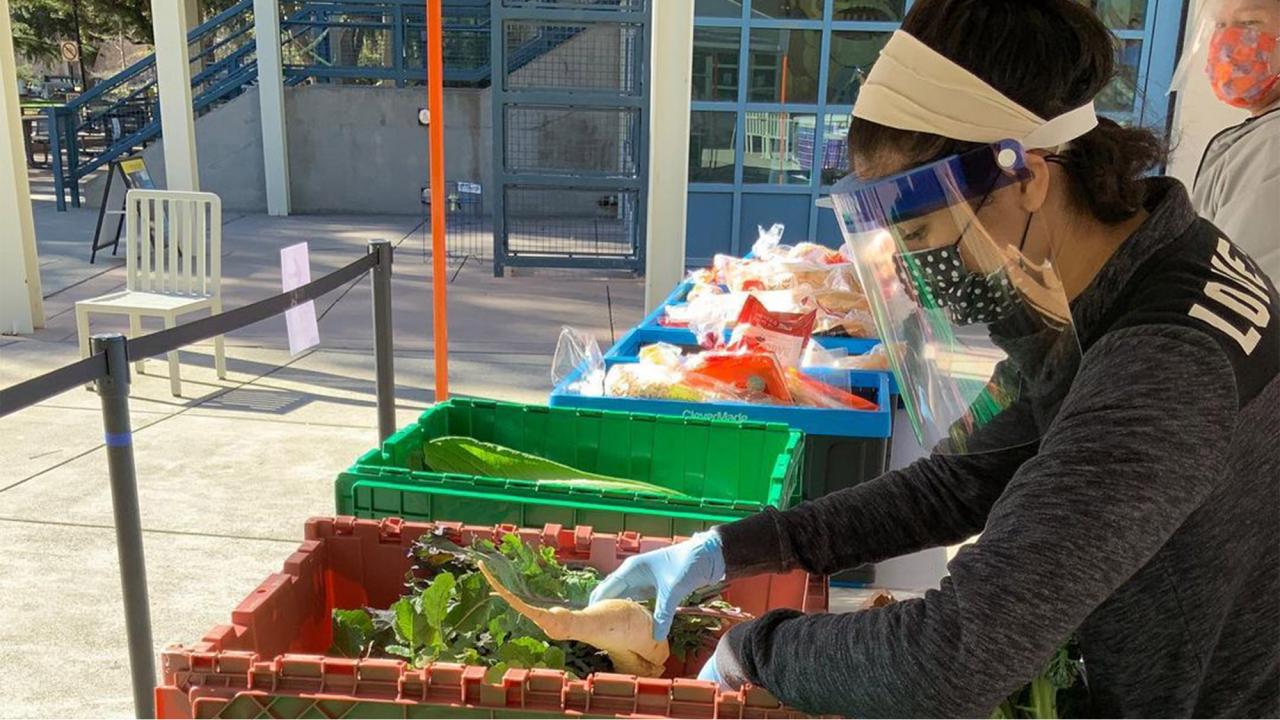 Student wearing face covering pulls vegetables out of large tote.