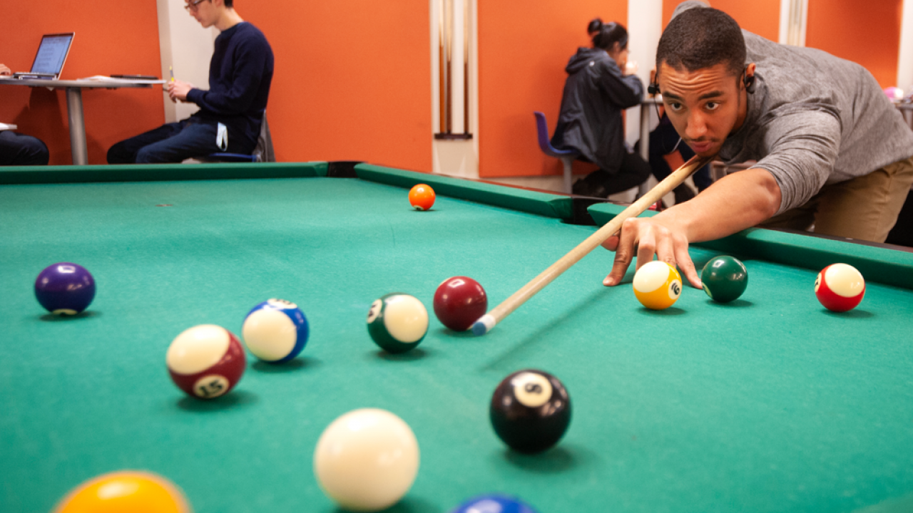 A male student plays pool in a common area at UC Davis