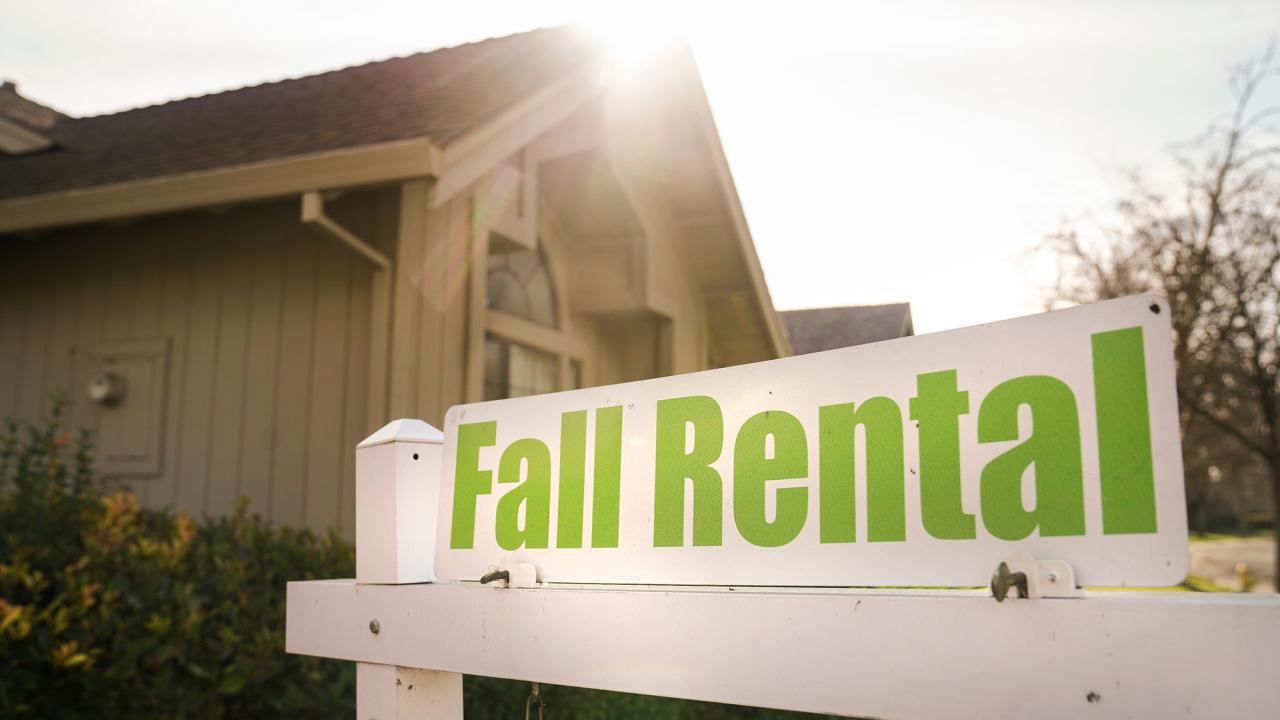 A white sign with "Fall Rental" in green lettering against part of an apartment building 