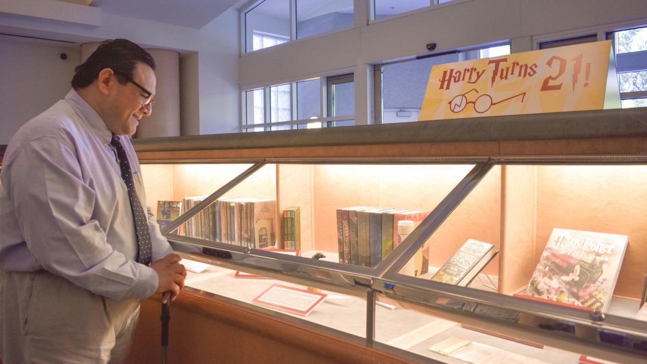 Man stands at exhibit case, obeserving the exhibit, "Harry Potter Turns 21"