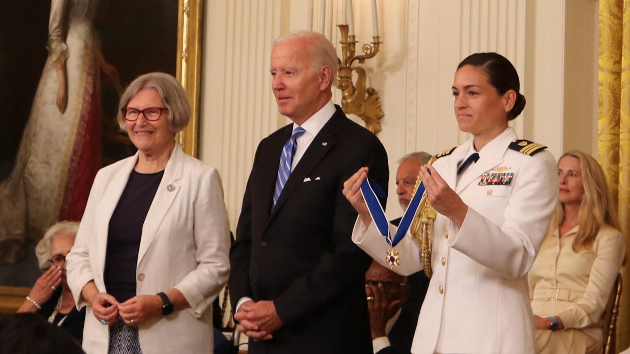 Sister Simone Campbell (in white blazer) and military aide (holding medal) flank President Joe Biden