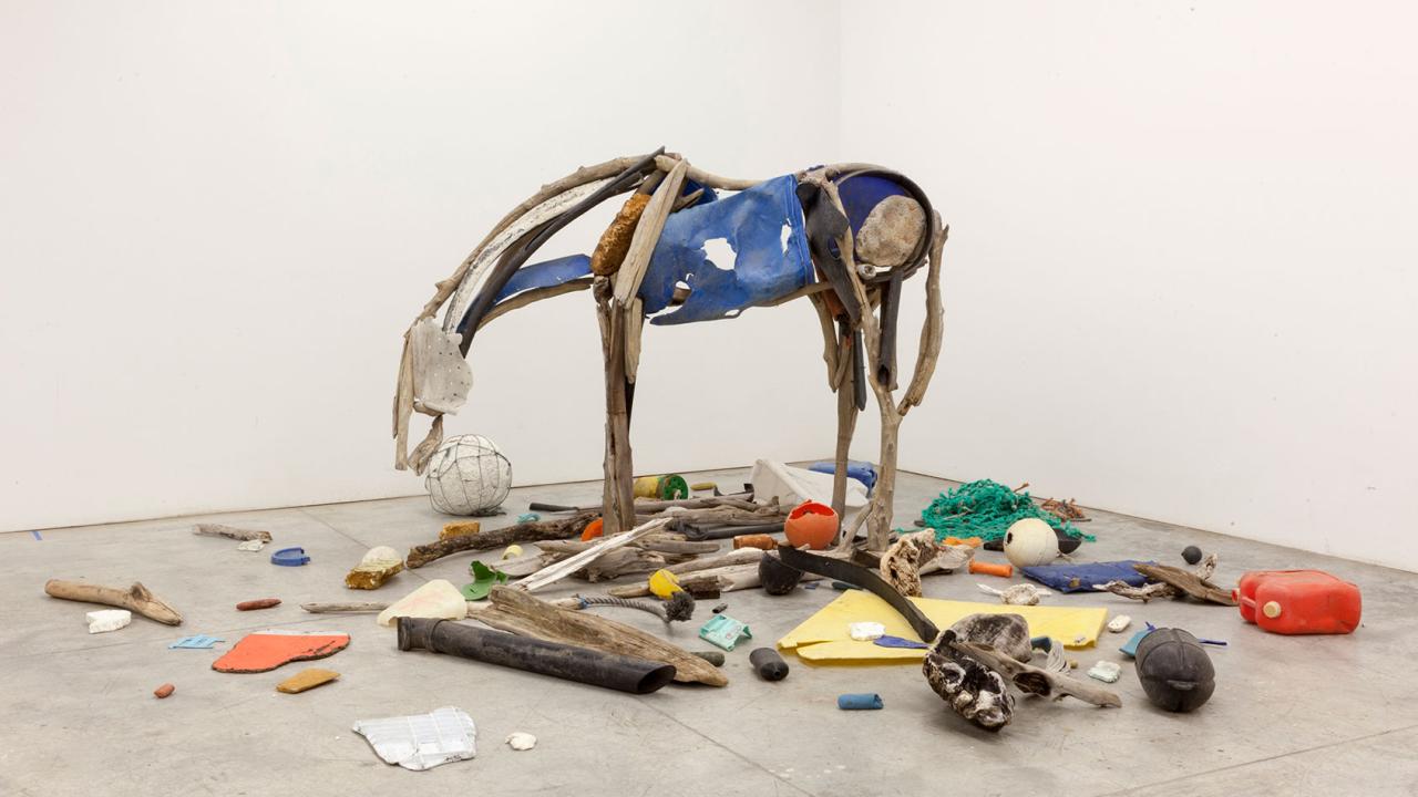 Sculpture of hollow horse in beige and blue with objects scattered below
