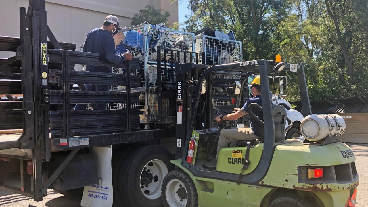 Items in metal containers are loaded onto a truck, by forklift.