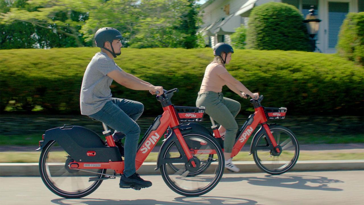 Two people ride red Spin bicycles.