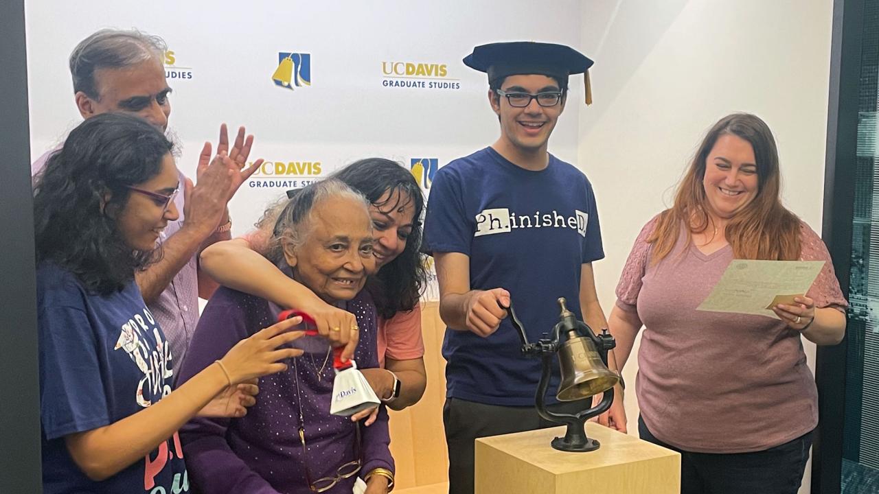 With four family members near him, Tanishq Abraham rings a bell to signify he has earned a doctoral degree.te