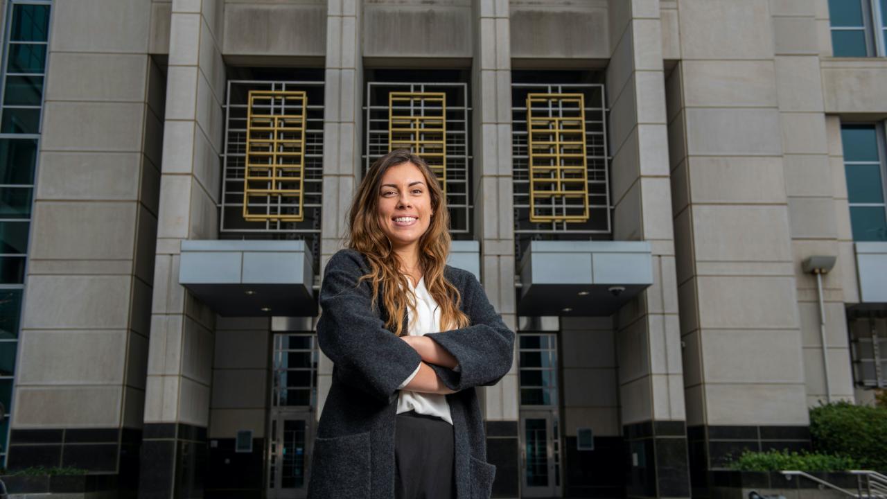 A student poses in front of a court building wearing a suit. 