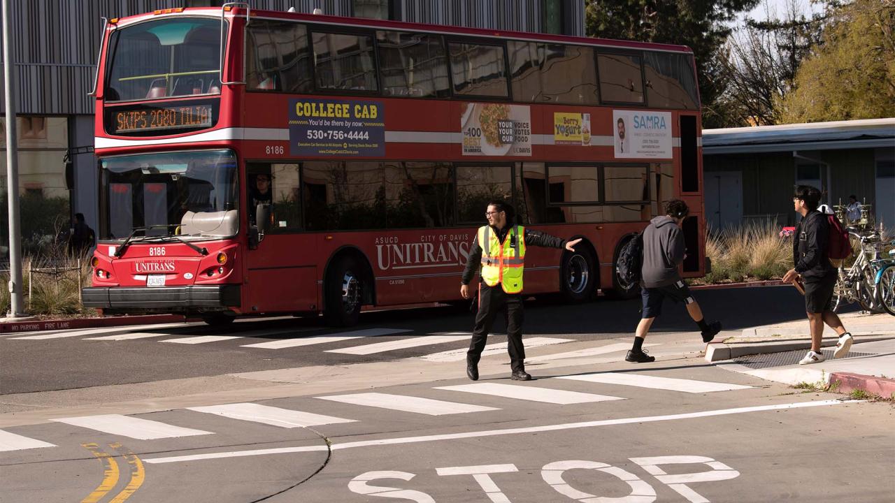 Crossing guard directing traffic, with red Unitrans bus in background.