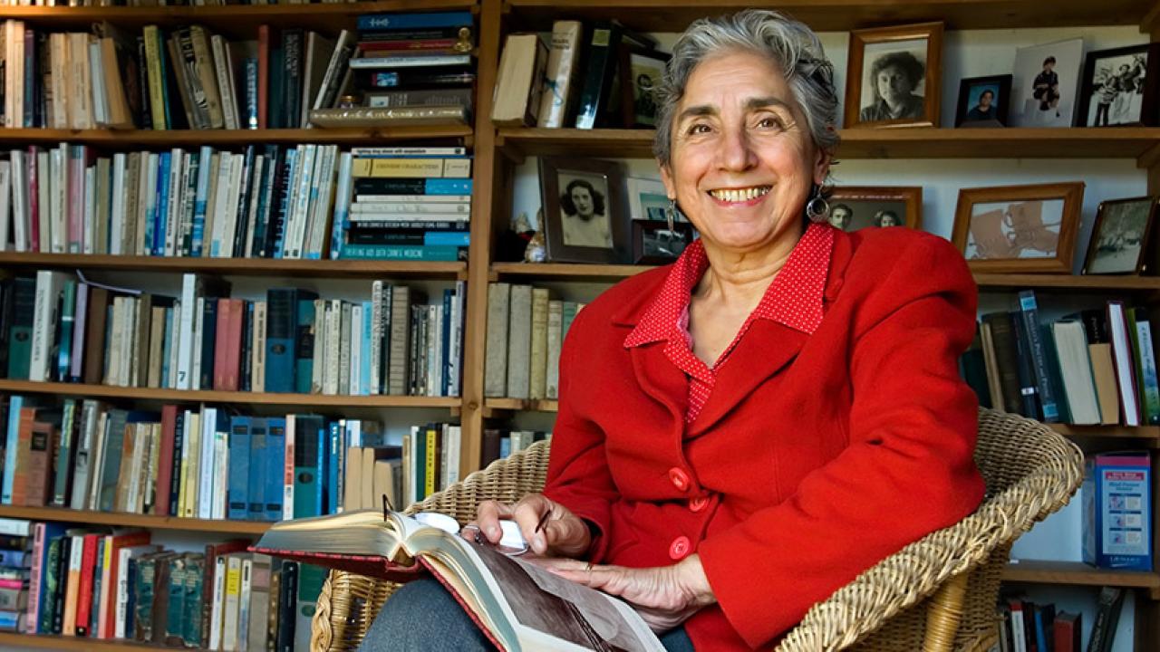 Brenda Schildgen in her book-lined library sitting with a book 