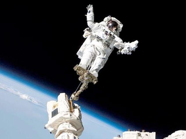 An astronaut floats in orbit connected to the space station by a small tether.