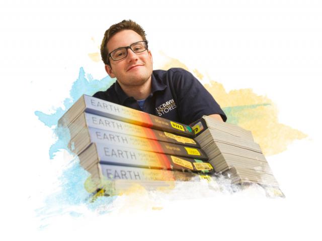 a male student smiling over a pile of books at the bookstore