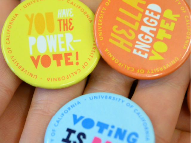handing hold different colored buttons each with a phrase about voting