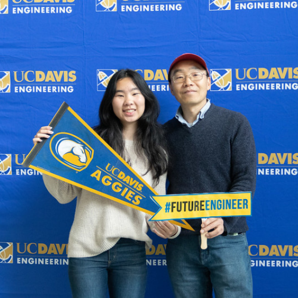 A student posing with a UC Davis pennant and their father