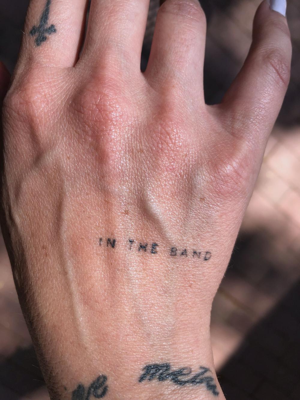 A hand tattoo shows the words 'in the band'
