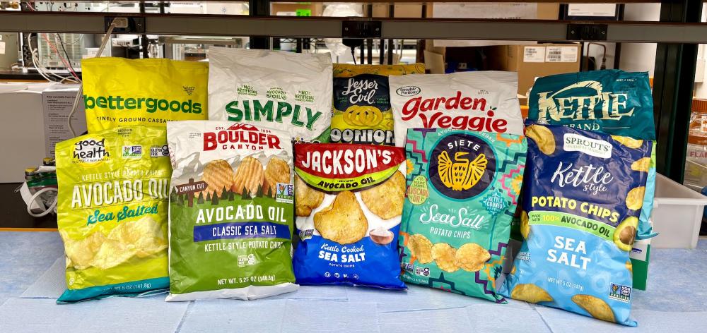 Assorted colorful chip and snack bags that claim they are made with avocado oil are lined on a table inside a lab. These chips were among the 54 avocado-labeled products tested in the Wang lab at UC Davis. (Selina Wang / UC Davis)