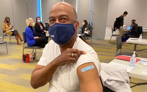 Chancellor Gary S. May rolls up his T-shirt sleeve, shows bandage over vaccination.