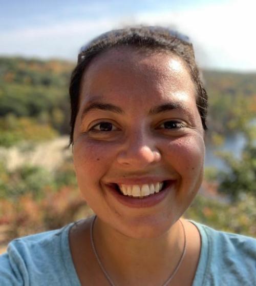 Headshot of scientist Anya Brown smiling with coastal landscape in bacckground