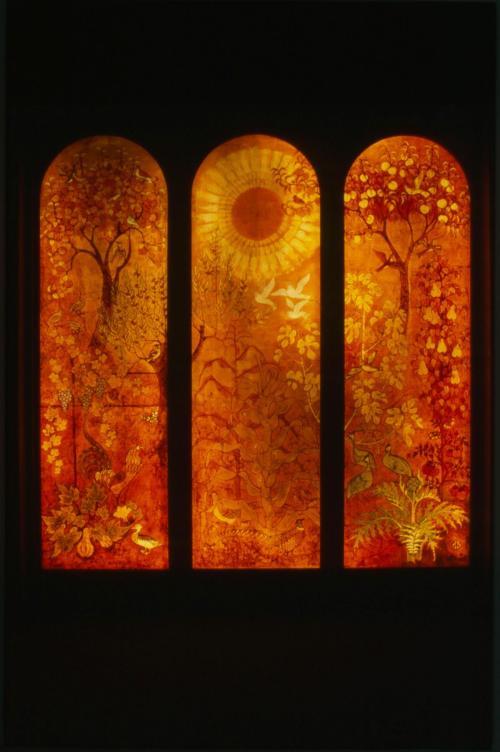 An orange-red batik panel depicting a sun, trees, plants, and birds across three arched windows.