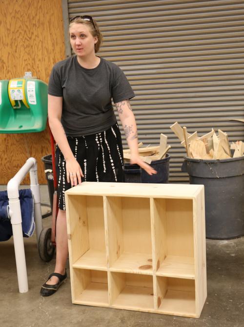 Woman displays furniture project (bookcase).