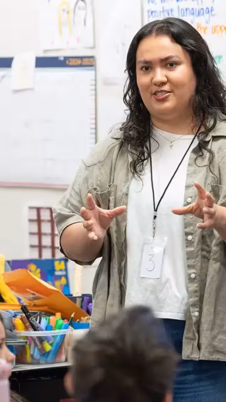 Teacher gestures while speaking to elementary students in a colorful classroom