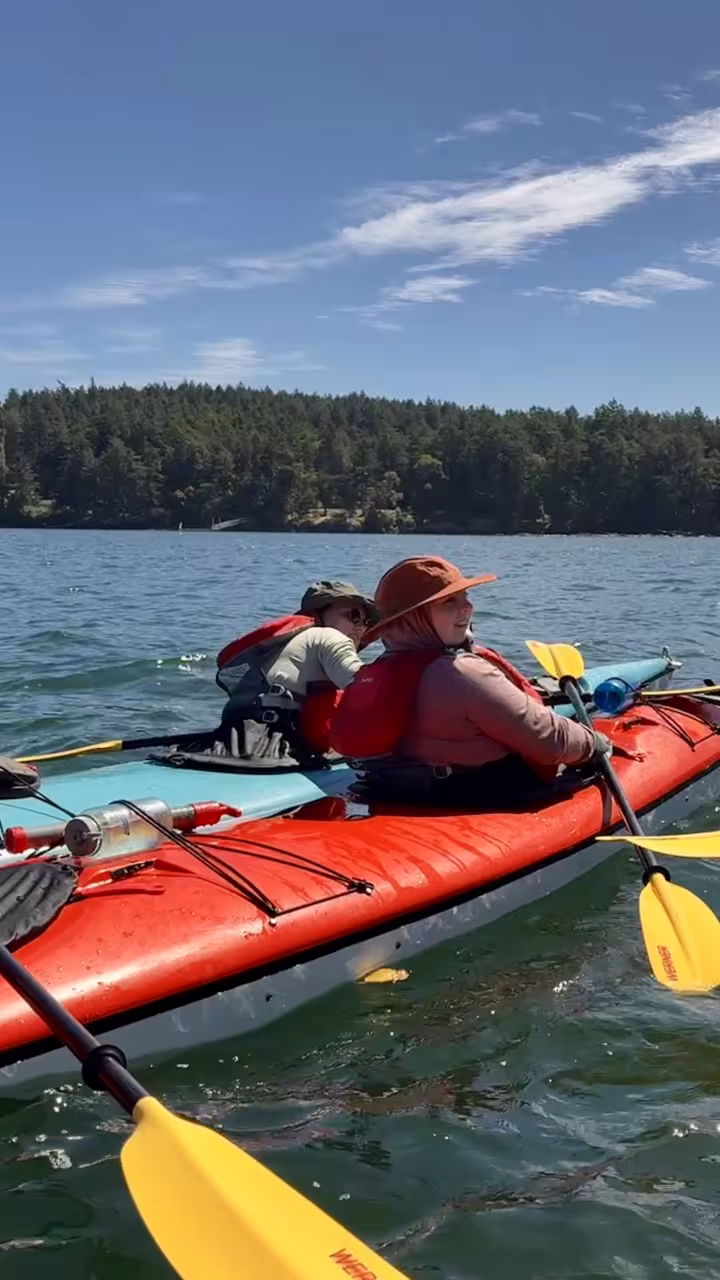 Group of kayakers in colorful kayaks on calm blue lake near forested shore