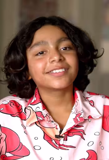 A smiling child with curly hair wearing a colorful crab-themed shirt.