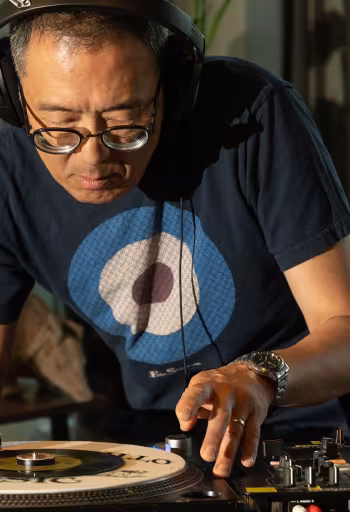 Man wearing headphones and blue target t-shirt adjusts vinyl on turntable in sunlit store
